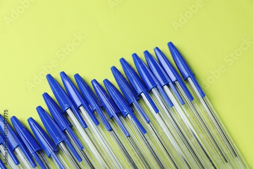 Many ballpoint pens with caps on light green background, flat lay