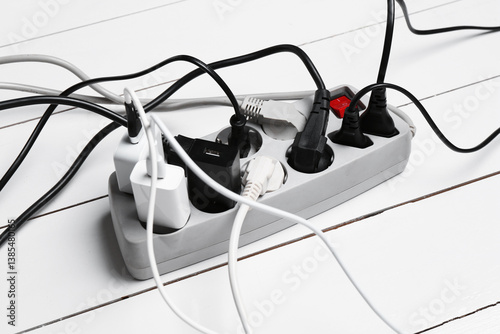 Extension power board overloaded with plugs on white wooden floor, closeup