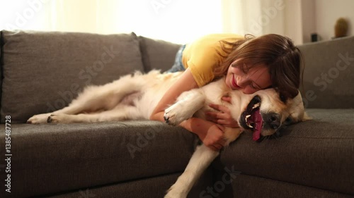 A cheerful teen girl is cuddling her golden retriever on a soft couch inside a bright living room. Sunlight streams in, creating a warm atmosphere as they enjoy each other's company.