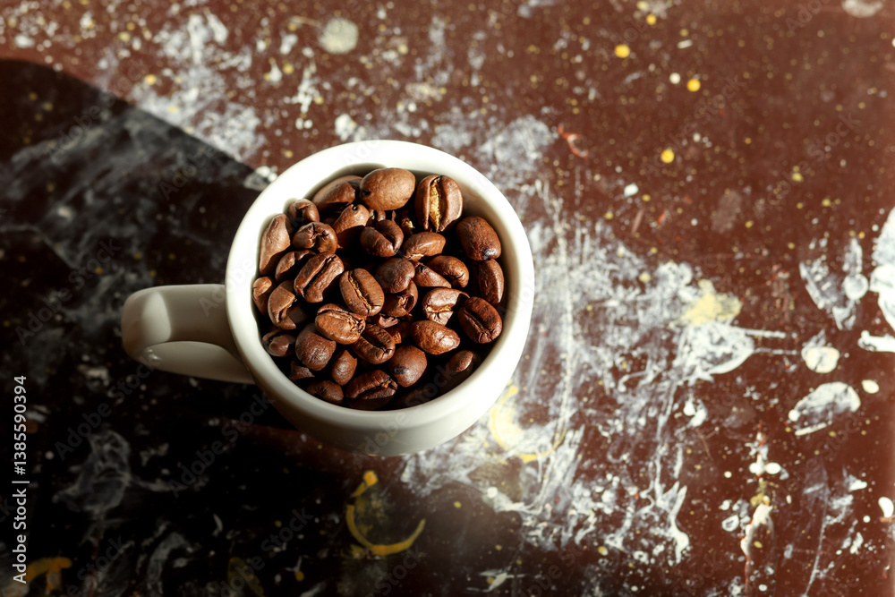 A creative coffee scene with a white cup tipped over, spilling a pile of coffee beans onto a brown and black background. Coffee art