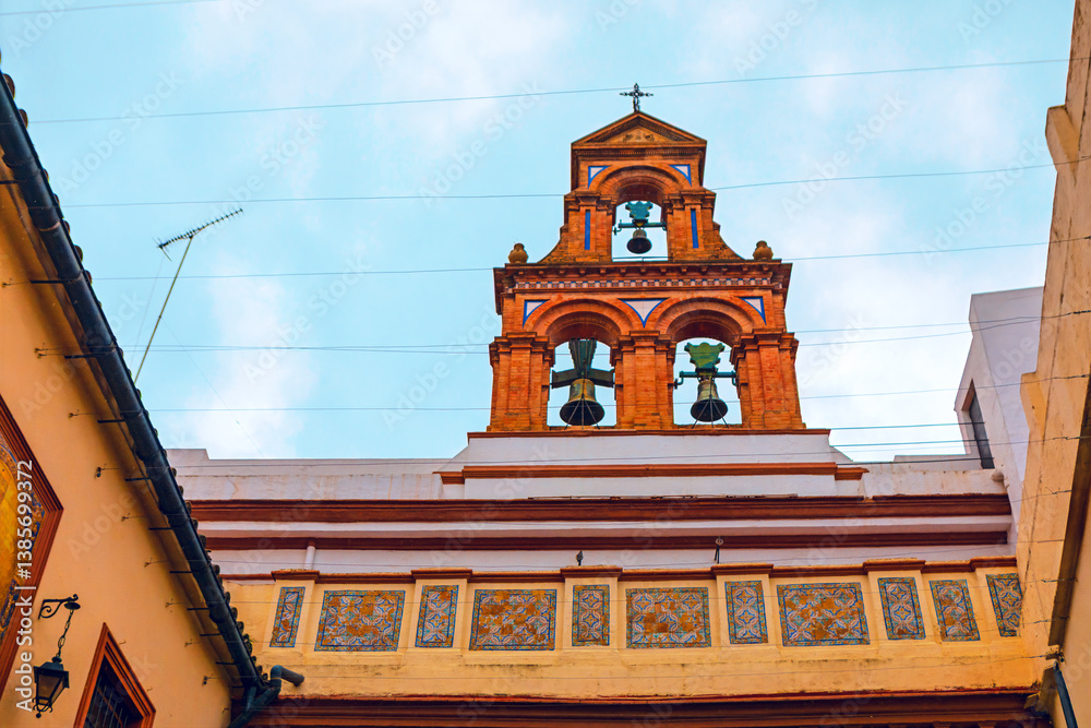 Bell tower adorned with three bells, standing out against a cloudy sky. Intricate tile work and a cross atop bell tower reflect the site cultural and historical significance