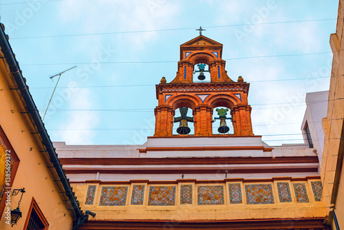 Obraz na płótnie Bell tower adorned with three bells, standing out against a cloudy sky. Intricate tile work and a cross atop bell tower reflect the site cultural and historical significance w salonie