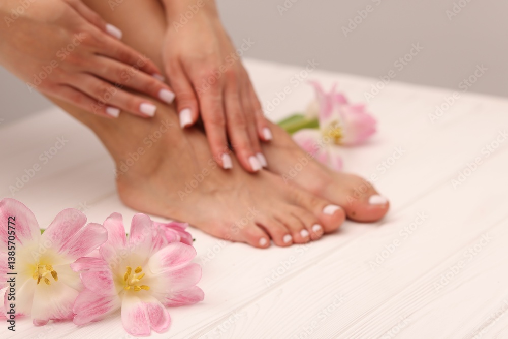 Woman showing neat toenails and fingernails after pedicure and manicure procedures and flowers on white wooden surface, closeup. Space for text Woman showing neat toenails and fingernails after pedicure and manicure procedures and flowers on white wooden surface, closeup. Space for text