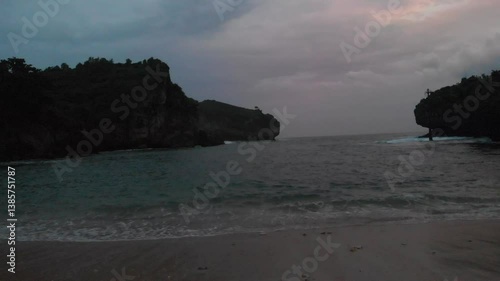 Coastal scene at twilight. Rocky cliffs meet ocean waves at a secluded beach