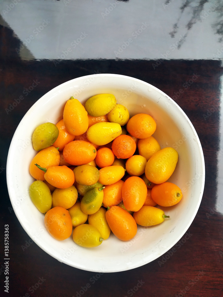 Kumquat Nagami in a white bowl against lacquered table with sky reflection Kumquat Nagami in a white bowl against lacquered table with sky reflection