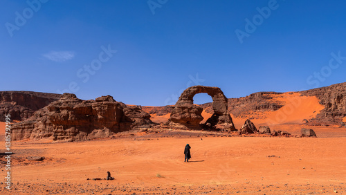One person and Arch in Tadrart Rouge, meaning Red Mountain, a mountain range in southeastern Algeria, part of the Algerian Desert providing massive dunes, rock formations and Martian landscapes