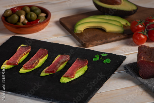 Obraz na płótnie Stone plate with slices of avocado topped with slices of mojama, accompanied by olives, avocado, and cherry tomatoes, a typical tapa from Andalusia. Close-up. w salonie
