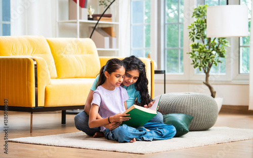 Happy Indian Asian mom and daughter bonding while reading a book on the floor at home