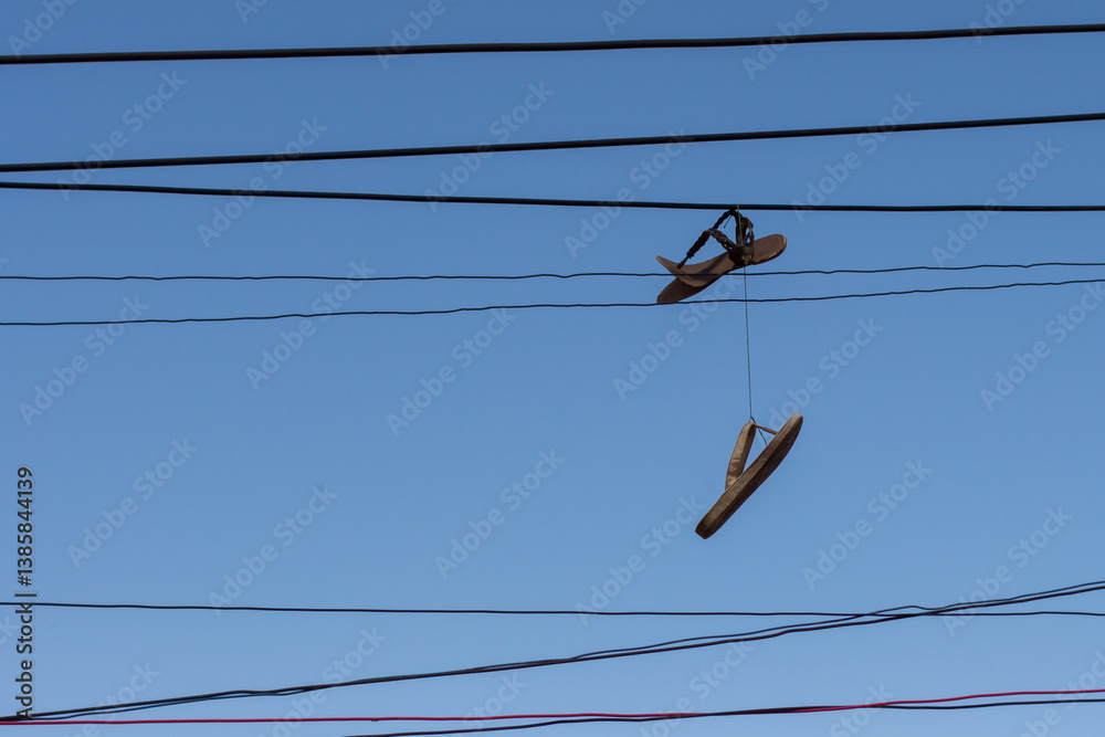 A pair of flip-flops dangling from electrical wires under a clear blue sky in Medellín, Medellin, Antioquia, Colombia. A quirky urban display evoking curiosity and reflection.