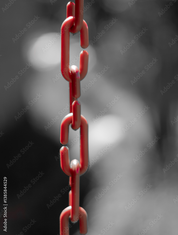Artistic composition with a red plastic chain and a black and white blurred background. Bokeh.