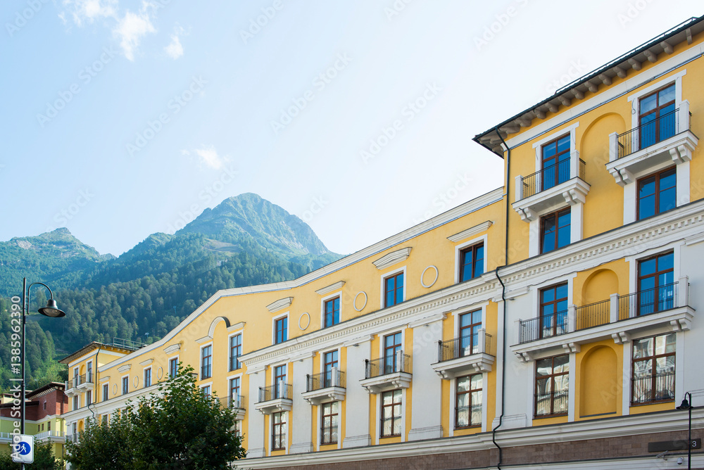 Fototapeta premium a beautiful low-rise yellow building with many windows against the backdrop of mountains in sunny weather