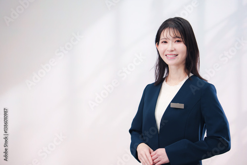 名札をつけて笑顔で接客をする若い女性（シンプル背景）