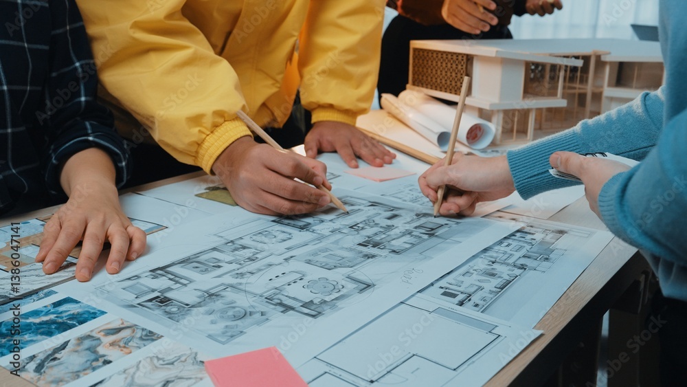 A collaborative atmosphere in an architecture office where multiple hands engage in sketching a detailed floor plan, surrounded by design materials and creative models. SACTR