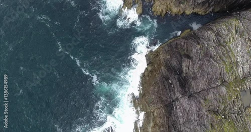 Waves crash on jagged wild ocean cliffs overhead drone view
