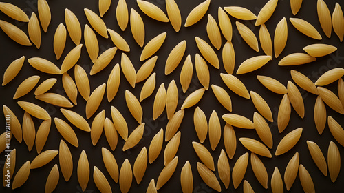 Close-up view of orzo pasta arranged in perfect rows on a dark, matte surface, with each rice-shaped grain reflecting light from various angles.