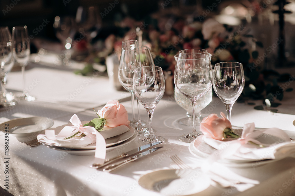 Elegant wedding table setting with a white tablecloth, white plates, light pink napkins, and delicate pink rose accents Elegant wedding table setting with a white tablecloth, white plates, light pink napkins, and delicate pink rose accents