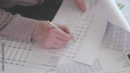 A detailed closeup of hands meticulously writing on financial spreadsheets and reports, showcasing data analysis