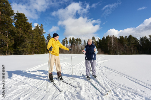 Taking short break from ski trip across snowy field, middle aged European couple enjoys sunny winter day.
