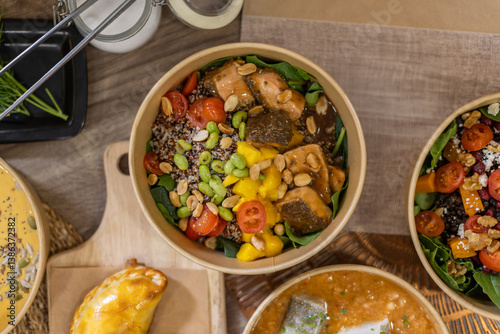 Fototapeta Naklejka Na Ścianę i Meble -  Overhead close-up of a vibrant poke bowl featuring quinoa, spinach, mango, cherry tomatoes, edamame, peanuts, and glazed salmon chunks. Artisanal takeout dish, compostable food box.
