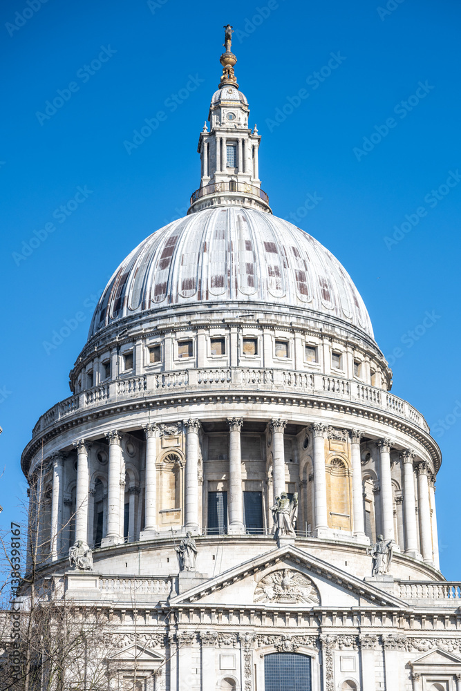 Obraz premium St. Paul's Cathedral in London features its impressive dome, showcasing intricate architecture against a clear blue sky. The iconic structure attracts many visitors throughout the day.