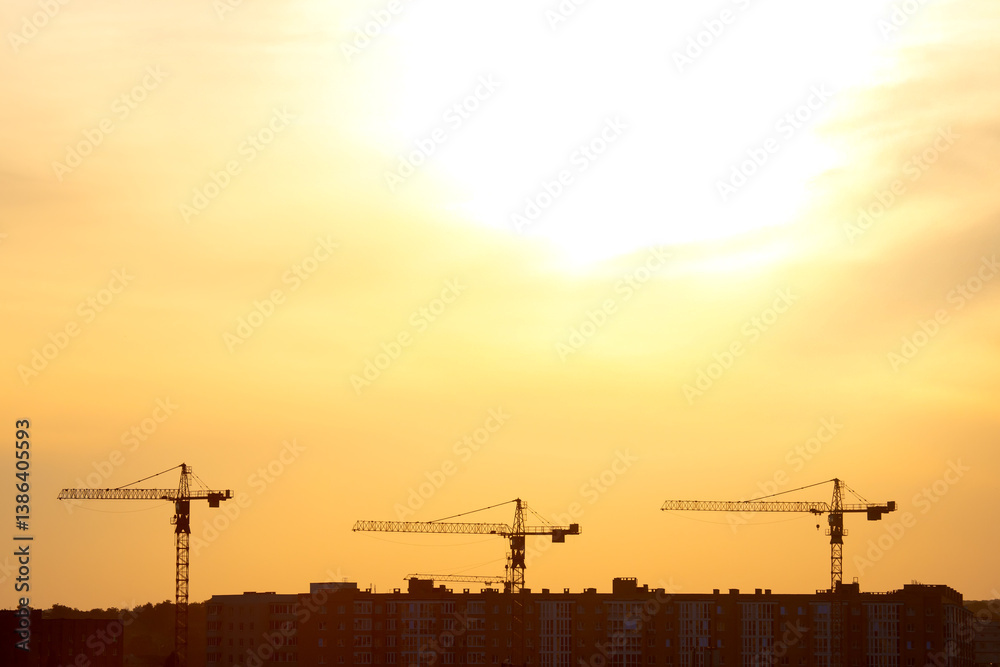 Silhouettes of three construction cranes against a golden sunset sky, with a city skyline of buildings in the background, capturing urban development at dusk. Silhouettes of three construction cranes against a golden sunset sky, with a city skyline of buildings in the background, capturing urban development at dusk.