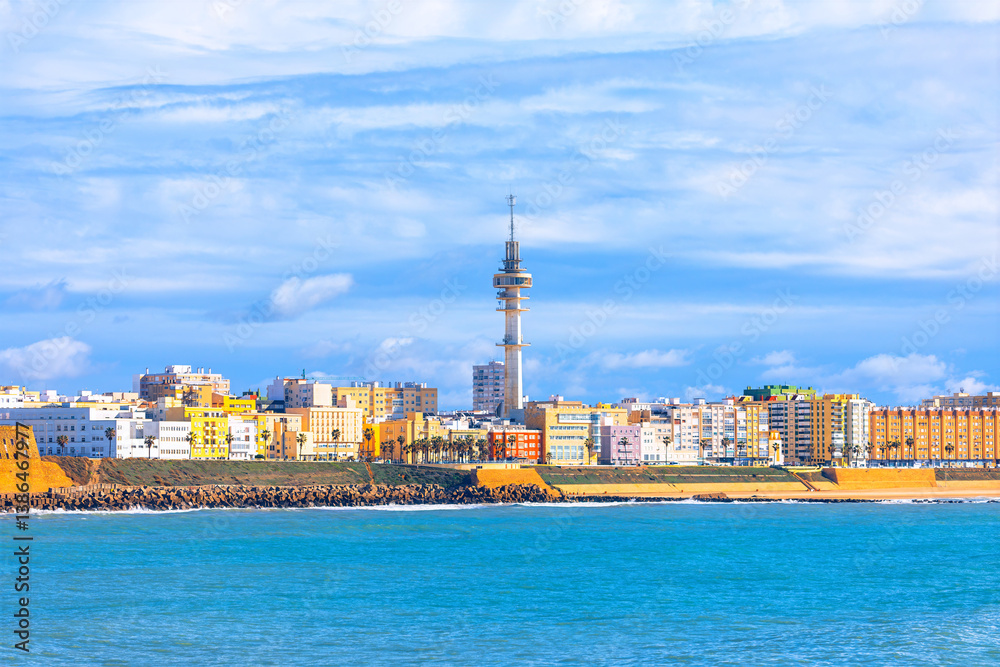 Colorful coastal cityscape of Cadiz, Spain, with the prominent Torre Tavira II rising above vibrant buildings. Calm sea and bright sky add to the scenic Atlantic Ocean charm