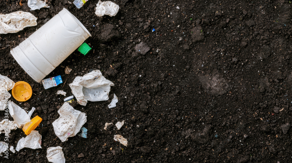 Obraz premium A discarded cup and crumpled papers lie on a dark, textured surface, highlighting litter and pollution.