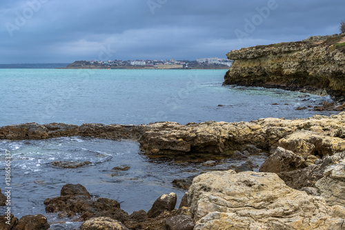 View of the rocky sea coast. Stones on the sea shore. Seaside town in the distance. Cloudy windy weather. Black Sea, Sevastopol, Crimea.