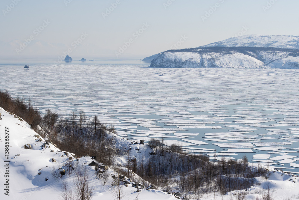 Spring drift of ice floes in Gertner Bay. Sea of Okhotsk. Magadan Region, Russia. Ice in the sea bay began to split and crack. Fishermen's cars were carried out to sea on broken-off ice floes.