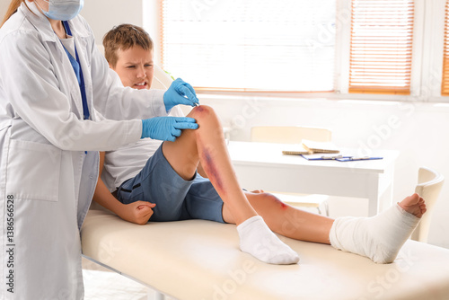 Obraz na plátně Female doctor treating little boy's wounded leg in clinic