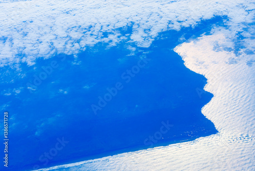 Stunning aerial view of a Morocco coastline partially veiled by clouds, with sunlight reflecting off the water and creating a shimmering effect. Shadowed African coast contrasted against a cloudy sky