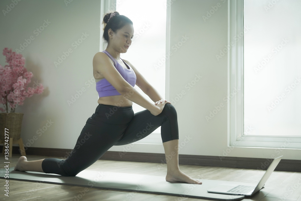 Obraz premium A woman is doing yoga poses in front of a laptop. She is wearing a purple top and black pants