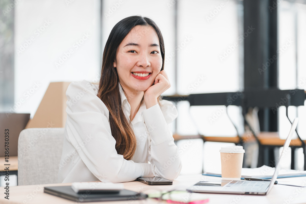 Confident businesswoman smiling at her desk with laptop, coffee cup, and documents in modern office setting. Confident businesswoman smiling at her desk with laptop, coffee cup, and documents in modern office setting.