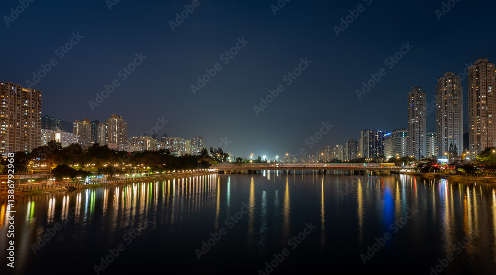Fototapeta premium A night view of Sha Tin city showing modern high rise housing development on both banks of the Shing Mum River. Hong Kong.