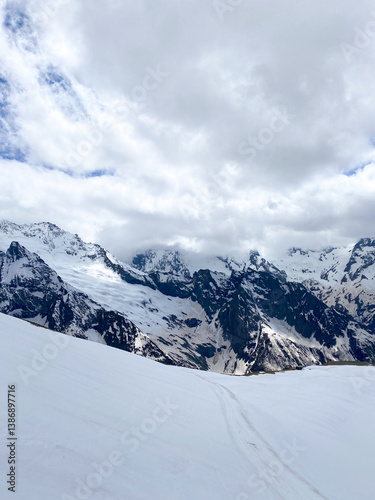Snow-capped mountains rise under a clear blue sky with fluffy clouds in a serene landscape of nature