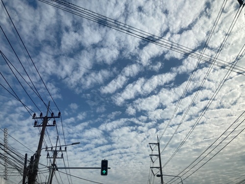 The view of the green light at the intersection, the electricity poles with the ้high-voltage power lines tangled together, and the clouds with tiger-like patterns on the bright, deep blue sky