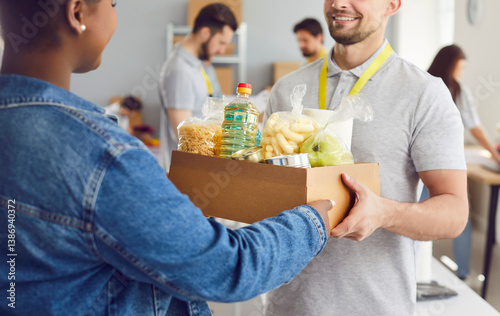 Close up shot of a happy Caucasian man volunteer handing a food box to an African American refugee woman at a humanitarian aid center. Essence of charity, assistance, donation and help.