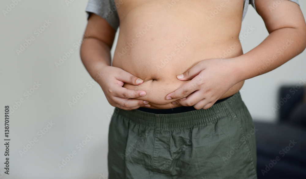 A fat child with a fat belly holds his stomach with his hands.