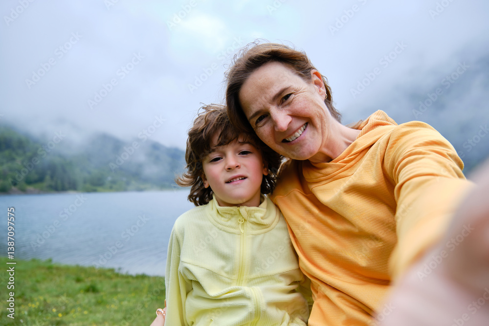 Obraz premium Happy mom and boy taking selfie against lake and mountains