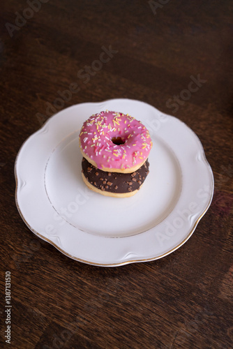Donuts with chocolate and pink icing on a white plate on a wooden table