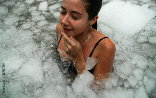 Woman practices cold therapy in an outdoor ice bath surrounded by tropical plants. A peaceful moment of self-care and healing