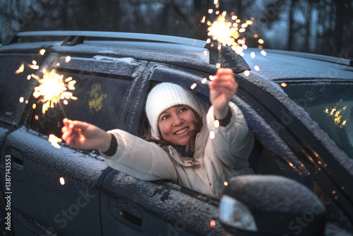 Young happy woman with sparkler in hands sitting in car on winter street in evening.