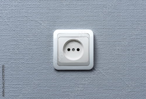 A white European-style electrical wall socket mounted on a textured light gray wall. The photo is minimalistic, centered, and well-lit.