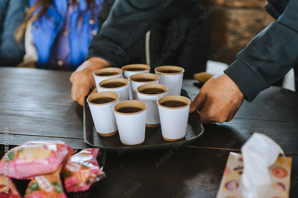 Waiter, server holding tray with paper cups of tea, coffee bringing to wooden table after order. Photo plan, takeaway food concept. Waiter, server holding tray with paper cups of tea, coffee bringing to wooden table after order. Photo plan, takeaway food concept.