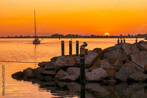 Sailboat approaching harbor entrance of Wiek at sunset over Wiek Bodden lagoon, Rügen, Mecklenburg-Vorpommern, Germany