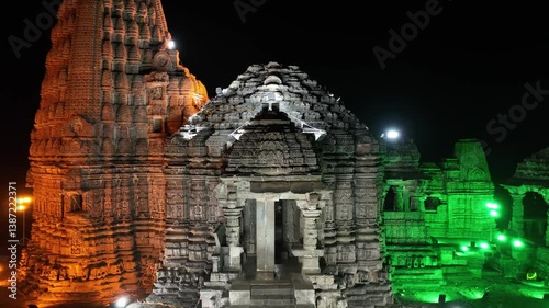 aerial night view of Gondeshwar Hindu temple of India illuminated in the colors of Indian flag: orange, white, green. saffron flag flies atop. stonework of temple is highlighted by strategic lighting