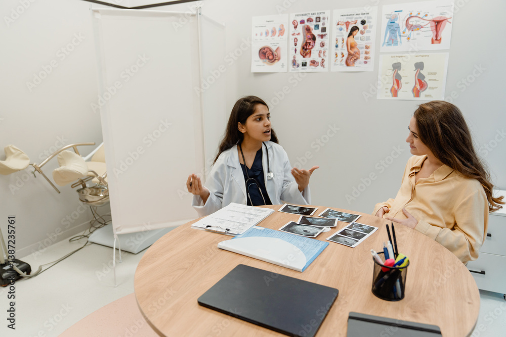 Obraz premium A young Indian female doctor in her late 20s, talking enthusiastically to her young, pregnant White female patient, as they sit in an office next to the desk that has x-rays of the baby on it