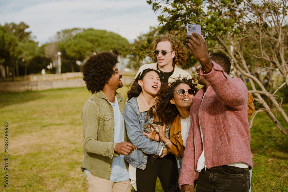 A Black man in his 20s in a pink jacket taking a selfie with a multiethnic group of friends in their 20s while they are standing next to each other in a park, laughing and posing with a dachshund A Black man in his 20s in a pink jacket taking a selfie with a multiethnic group of friends in their 20s while they are standing next to each other in a park, laughing and posing with a dachshund