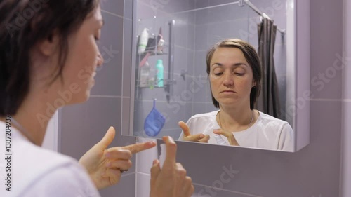 Woman applying eye cream on eyelids and under eyes in bathroom, skincare and beauty routine for healthy skin.