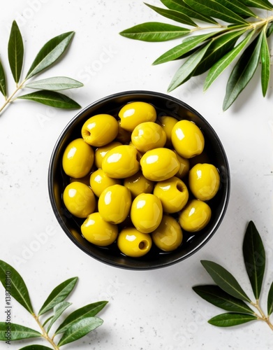 Fresh green olives in a black bowl with olive leaves on a light countertop